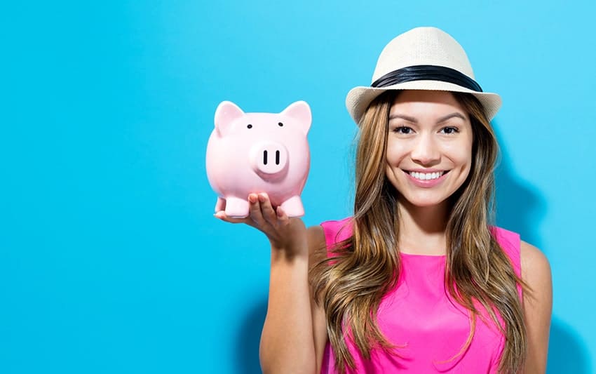 Cute young woman holds up a pink piggy bank while showing off her smile. 